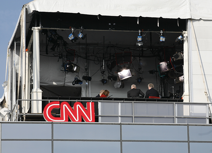 Photographie d'un studio de CNN au Canada en haut d'un bâtiment. Le studio est sous une tente blanche ouverte, on voit plusieurs personnes attablées, des projecteurs dirigées vers elles. 
