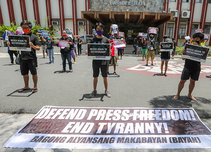 Photographie d'une manifestation contre le gouvernement philippin organisée par des membres du parti de gauche Bagong Alyansang Makabayan. Ils tiennent des pancartes promouvant la liberté de la presse, devant eux, au sol, une affiche "Defend Press Freedom! End Tyranny!" 
